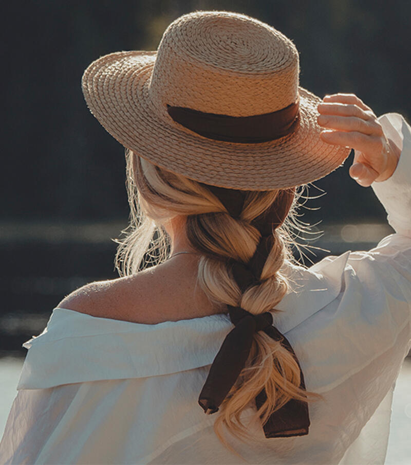 Kvinna bakifrån med en hatt och isättning av Cendre Ash Blond Mix Braid Extension framför havet